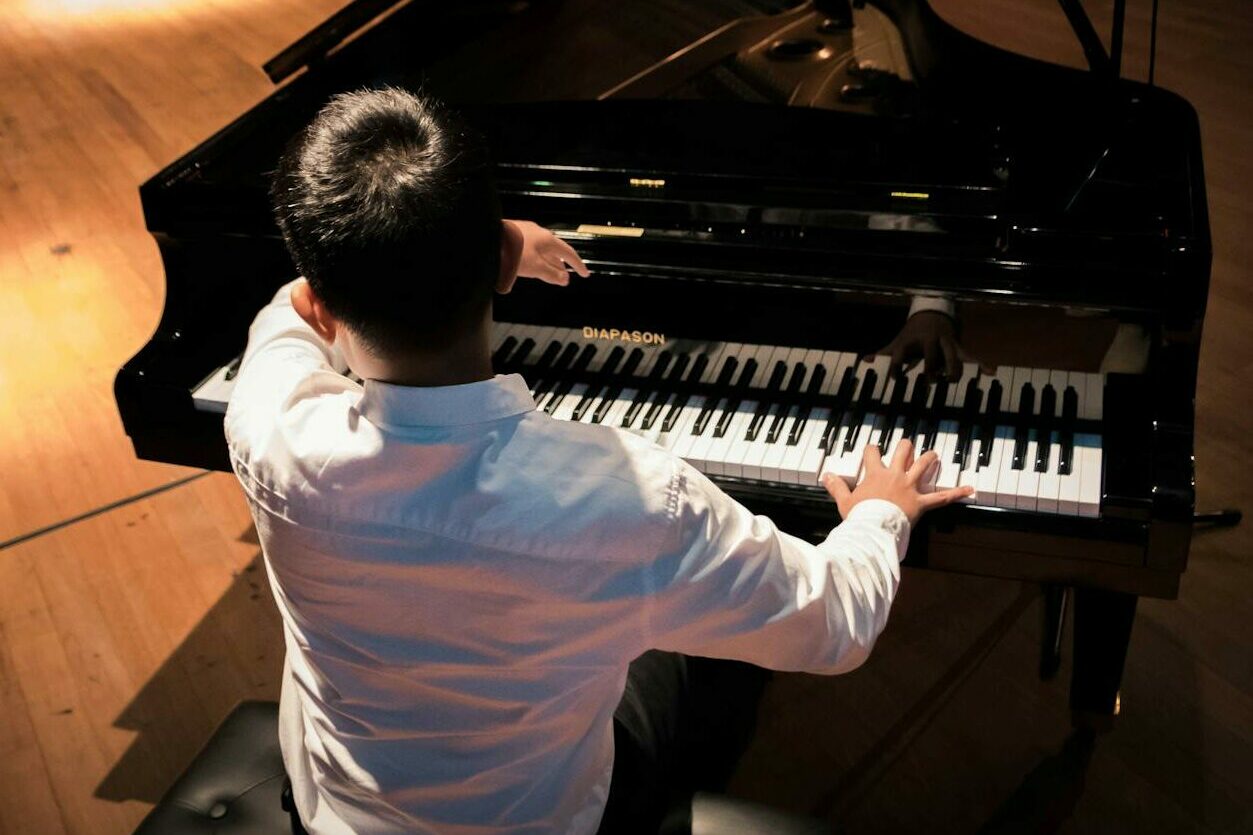 back view photo of a man playing a black grand piano